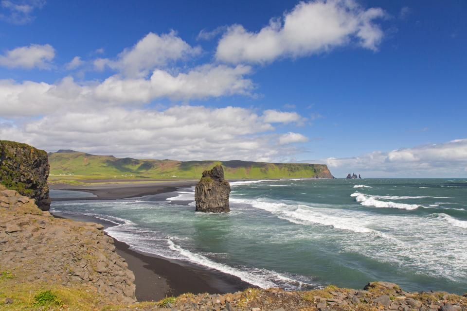 A big rock juts out from the ground in the sea along a beach in Iceland