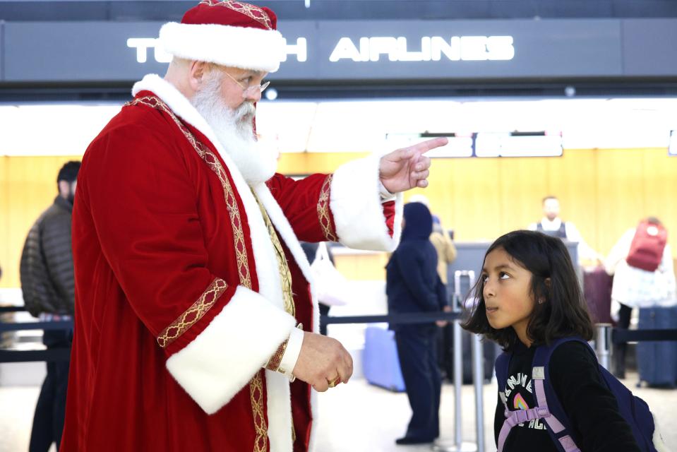 DULLES, VIRGINIA - DECEMBER 21: A man dressed as Santa Claus greets a young passenger at Dulles International Airport on December 21, 2023 in Dulles, Virginia. AAA predicted that this travel season will be the second-busiest holiday travel season since 2000.