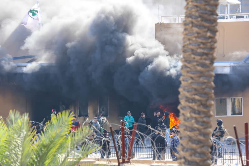 Attackers and assailants set fire to a gate as smoke rises from inside the compound of the U.S. embassy in Baghdad