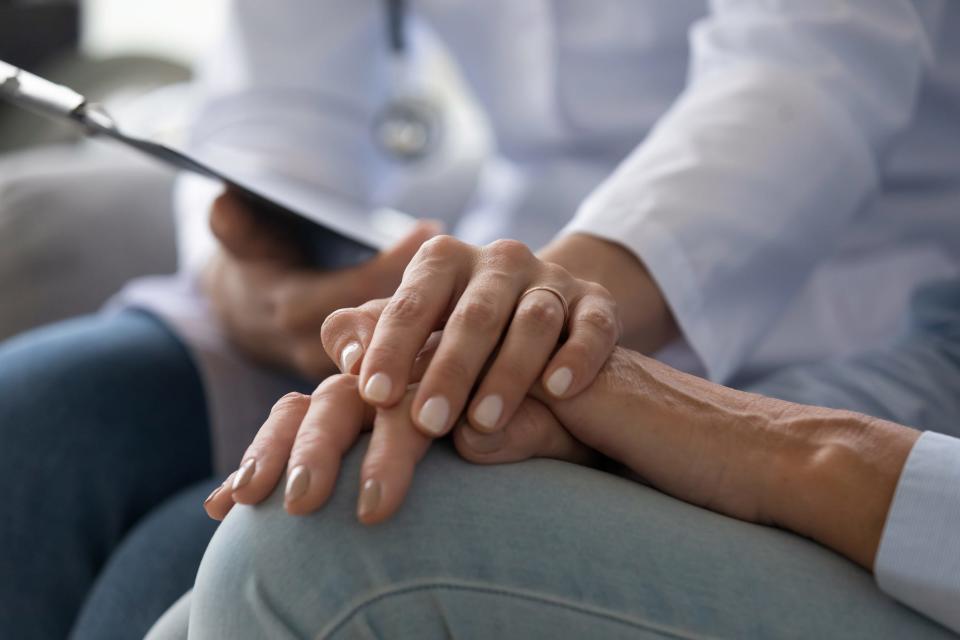 Nurse wearing white medical uniform holding hand of female patient.