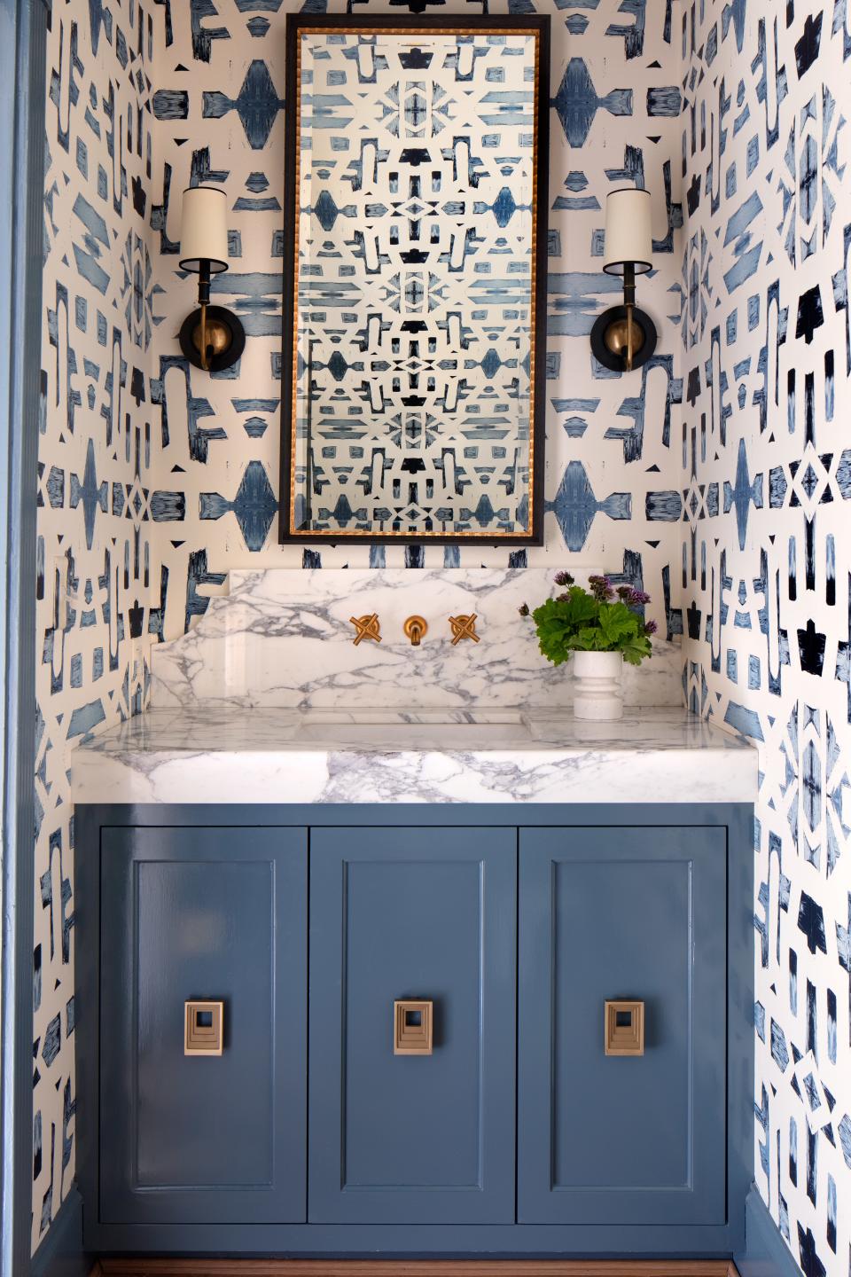 In the powder room, a soothing blue Indigo Ocean Alta Non-Woven wallpaper by Lindsay sets a calming tone. A custom vanity is bejeweled in Nest Studio pulls, and Circa Lighting sconces flank a custom mirror.