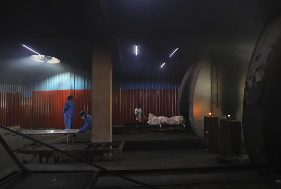 Workers remove a stretcher as others prepare to cremate the body of a COVID-19 victim in New Delhi, India, Wednesday, Sept. 16, 2020. (AP Photo/Manish Swarup)