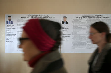 People walk past a broadsheet with information about candidates Petro Poroshenko and Volodymyr Zelenskiy at a polling station during the second round of a presidential election in Kiev, Ukraine April 21, 2019. REUTERS/Viacheslav Ratynskyi