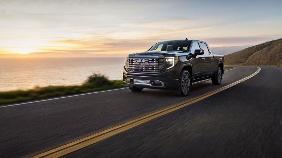 2024 gmc sierra denali ultimate 1500 crew cab short box in titanium rush metallic with 7 spoke ultra bright machined wheels 34 driver side front view in motion next to water