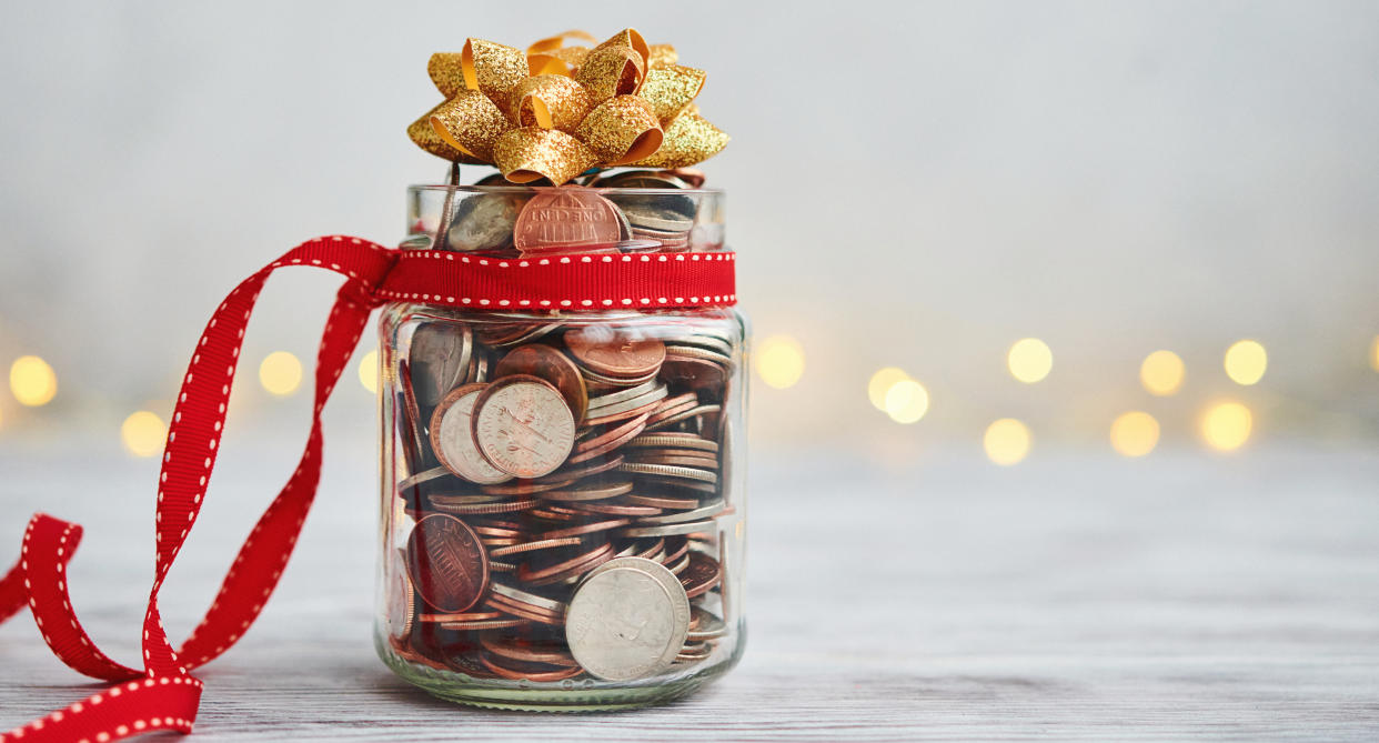 A see through jar with pennies in it sits on a table wrapped in Christmas ribbon and a bow on top. (Getty Images)