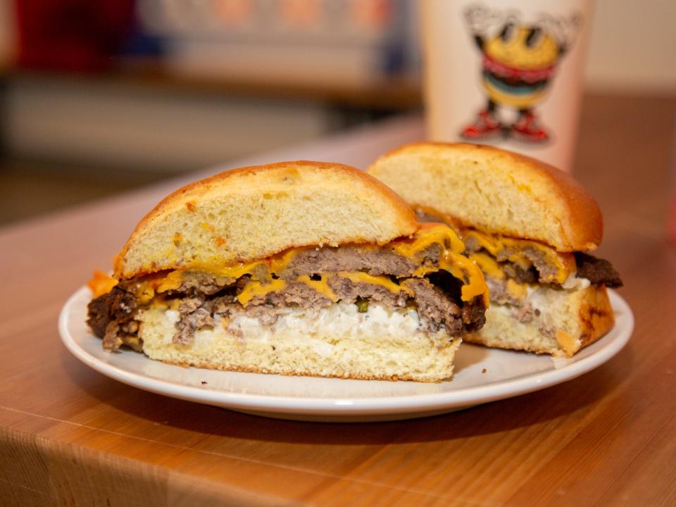 A burger on a paper box with a cup in the back.