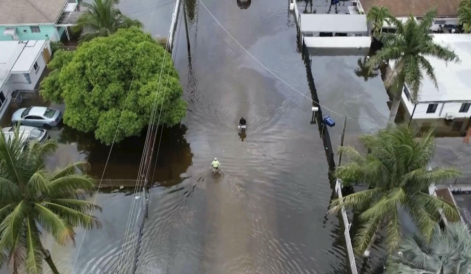 This aerial view taken from video shows people walking on a flooded street in Northeast Miami-Dade County, Fla., on Thursday, June 13, 2024. A tropical disturbance brought a rare flash flood emergency to much of southern Florida the day before. Floridians prepared to weather more heavy rainfall on Thursday and Friday. (AP Photo/Daniel Kozin)