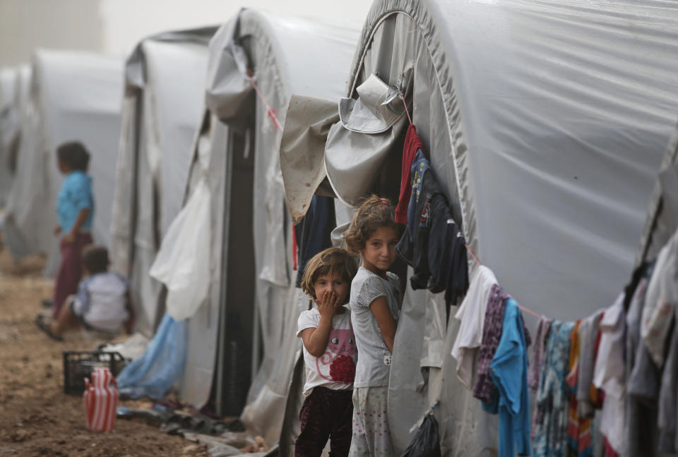 FILE - In this Oct. 11, 2014 file photo, Syrian Kurdish refugee children who fled Kobani with their families stand outside their tent at a refugee camp in Suruc, on the Turkey-Syria border. Syria’s Kurds have been America’s partner in fighting the Islamic State group for nearly four years. Now they are furious over an abrupt U.S. troop pull-back that exposes them to a threatened attack by their nemesis, Turkey. The surprise U.S. pull-back from positions near the Turkish border, which began Monday, Oct. 7, 2019, stung even more because the Kurds have been abandoned before by the U.S. and other international allies on whose support they'd pinned their aspirations. (AP Photo/Lefteris Pitarakis, File)