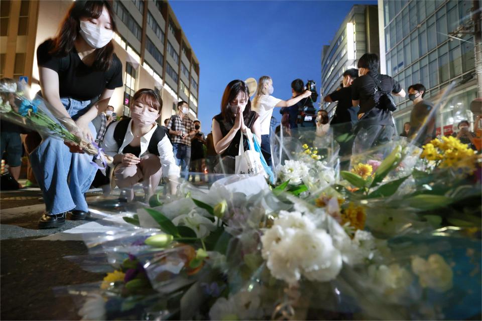 People pray at a makeshift memorial at the scene where the former Prime Minister Shinzo Abe was shot while delivering his speech to support the Liberal Democratic Party's candidate during an election campaign in Nara, Friday, July 8, 2022. Abe, a divisive arch-conservative and one of his nation's most powerful and influential figures, has died after being shot during a campaign speech Friday in western Japan, hospital officials said.(Kyodo News via AP)