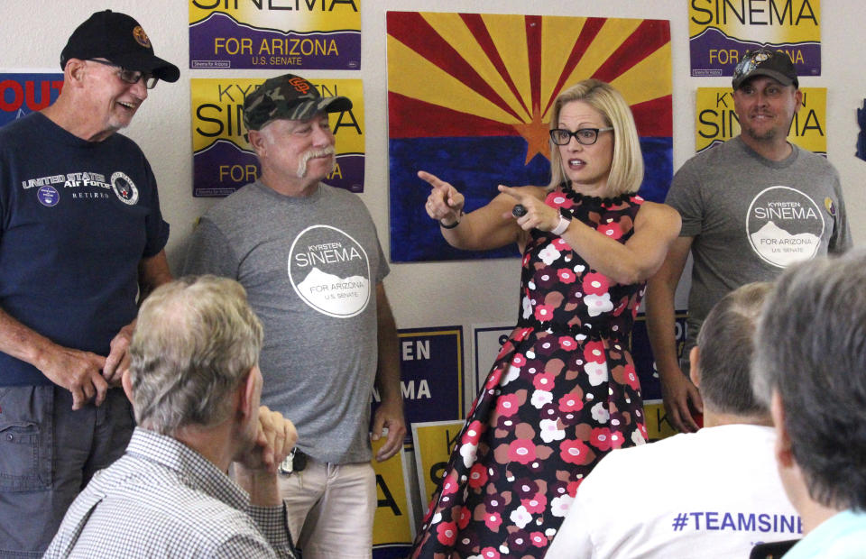 Kyrsten Sinema points her fingers forward while standing near half a dozen others, some of whom wear T-shirts that read: Krysten Sinema for Arizona U.S. Senate.