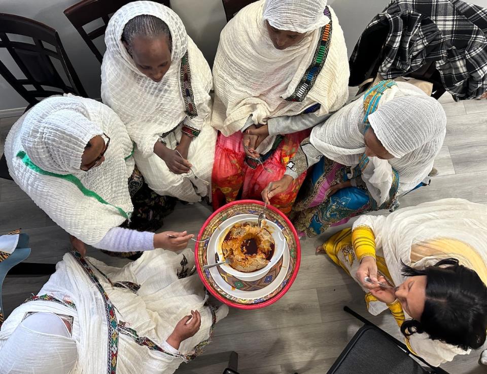 Women share a taste of the traditional Ethiopian barley porridge as part of the celebration for a new mother in Calgary. 