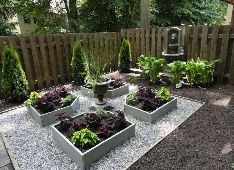 Four raised garden beds surrounded by gravel, with a decorative plant in the middle of the area