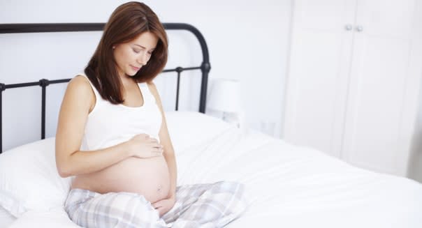 A pregnant woman sitting on her bed and holding her exposed baby bump