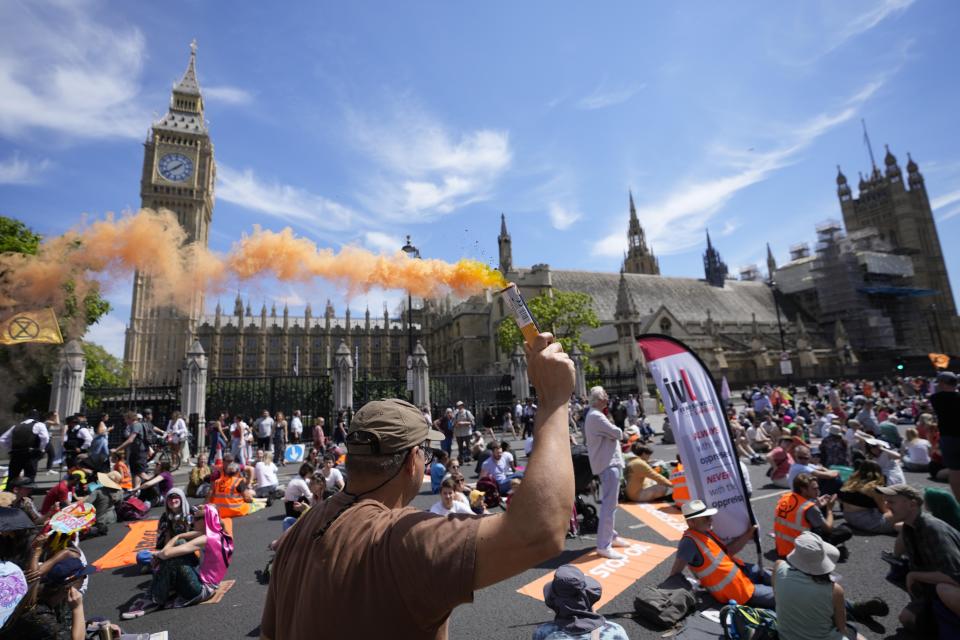 An activist burns a flare during a demonstration against the climate change, in Parliament Square, London, Saturday, July 23, 2022. (AP Photo/Alessandra Tarantino)