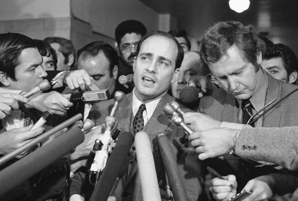 A man speaks, with a lot of microphones near his face.