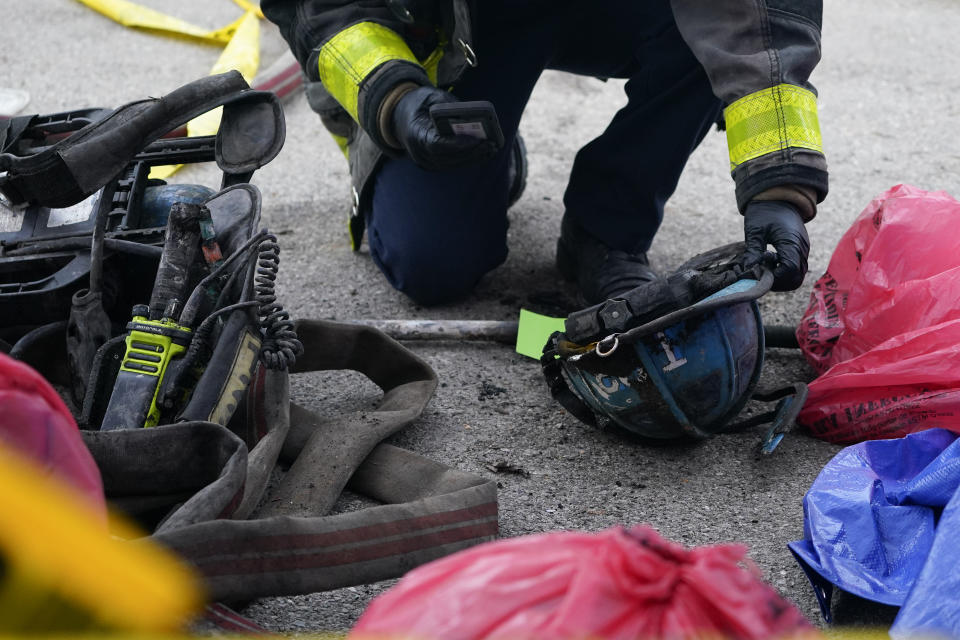 An official takes cellphone images of a helmet and equipment belonging to firefighters and collected from the site of a building collapse while battling a two-alarm fire in a vacant row home, Monday, Jan. 24, 2022, in Baltimore. Officials said several firefighters died during the blaze. (AP Photo/Julio Cortez)