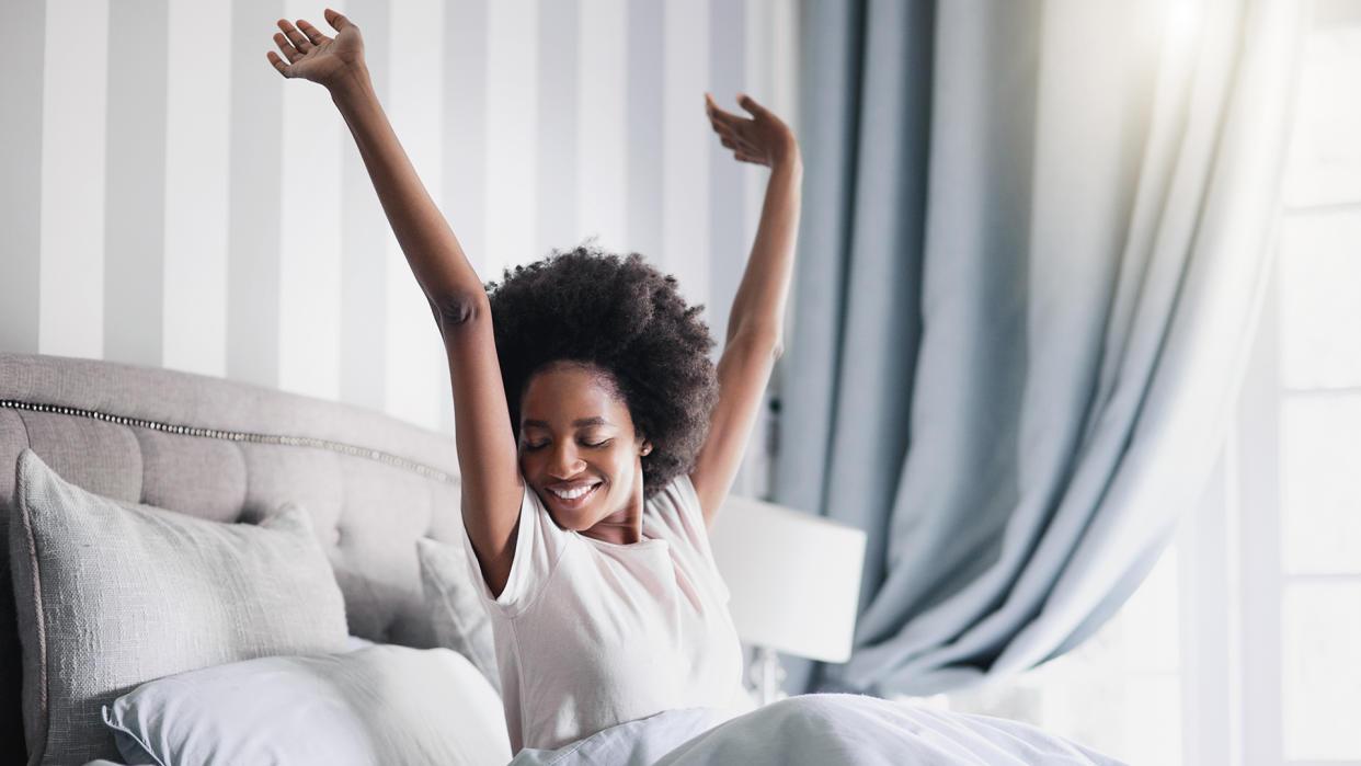  A woman wakes up and stretches on her bed in a bedroom. 