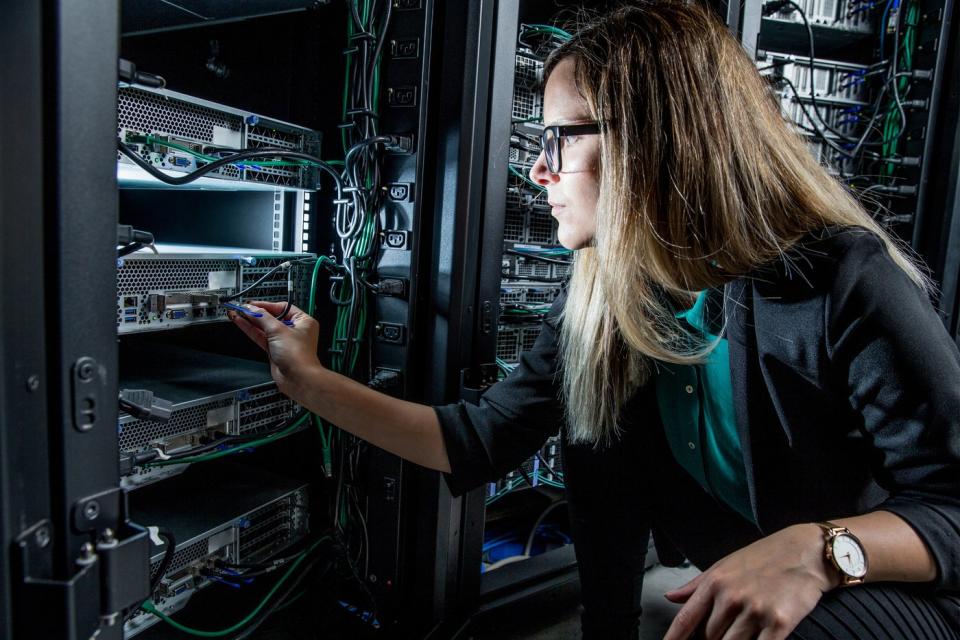 An engineer checking wires and switches on a data center server tower. 