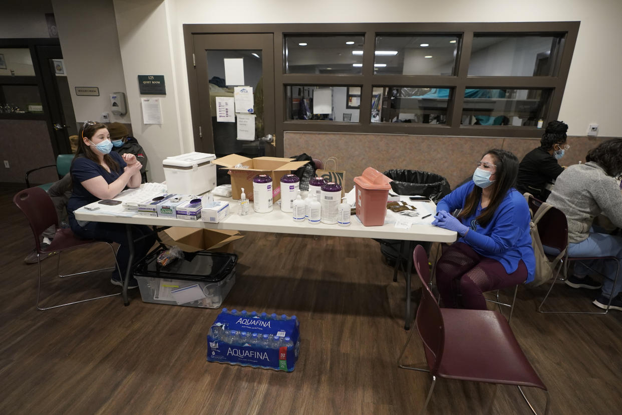 Aurora Artman, right, a medical assistant at Harborview Medical Center, talks with a colleague as they work Wednesday, April 7, 2021, at a COVID-19 vaccination clinic set up at a YWCA shelter for women lacking housing in Seattle. Homeless Americans who have been left off priority lists for coronavirus vaccinations — or even bumped aside as states shifted eligibility to older age groups — are finally getting their shots as vaccine supplies increase. (AP Photo/Ted S. Warren)