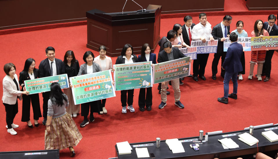 立法院長韓國瑜在立法院敲槌三讀通過「地方民意代表費用支給及村里長事務補助費補助條例」，國民黨委員（右）、民進黨委員（左）等朝野立委，不約而同舉標語合影見證。記者曾學仁／攝影