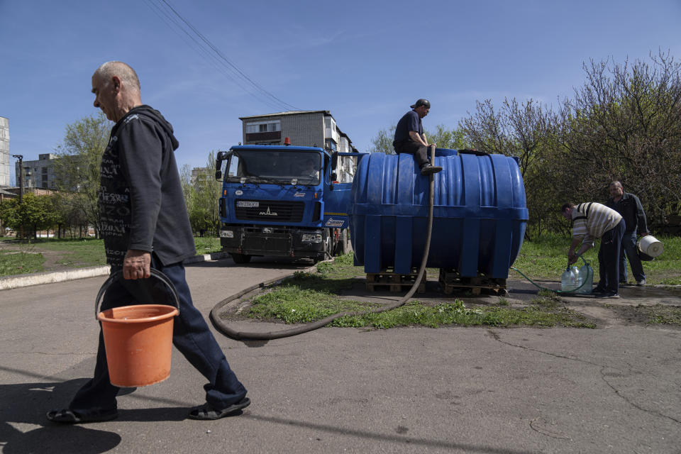 Local residents fill cans with water from a water tank installed for residents of Toretsk, eastern Ukraine, Monday, April 25, 2022. Toretsk residents have had no access to water for more than two months because of the war. (AP Photo/Evgeniy Maloletka)