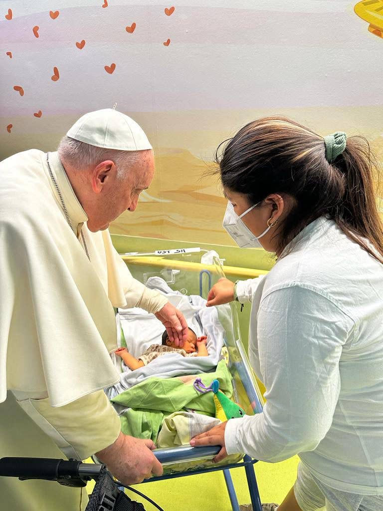 In this image made available by Vatican Media, Pope Francis caresses an infant before baptising him with the name of Miguel Angel, Friday, March 31, 2023 inside the Agostino Gemelli University Hospital where he is treated since Wednesday for a bronchitis. Francis is expected to be discharged on Saturday. (AP Photo/Vatican Media)