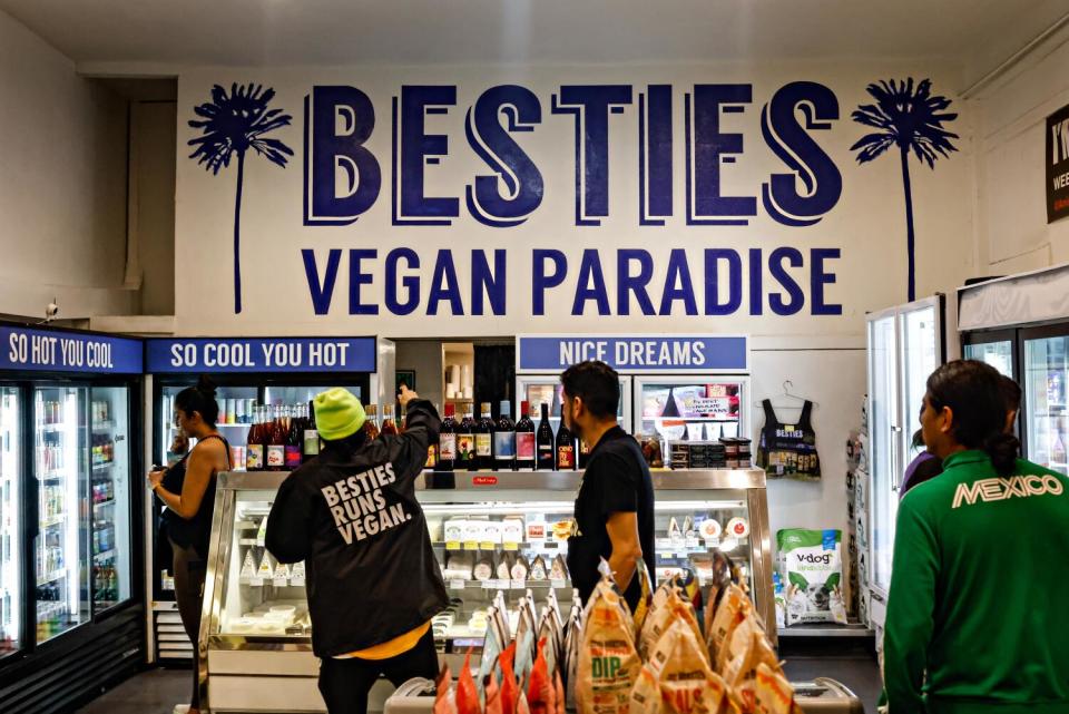 People stand at a counter in a store with the words Besties Vegan Paradise on the wall above them