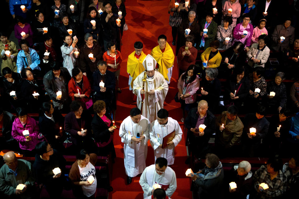 FILE - In this Saturday, March 31, 2018, file photo, Chinese Bishop Joseph Li Shan, center, walks down the aisle during a Holy Saturday Mass on the evening before Easter at the Cathedral of the Immaculate Conception, a government-sanctioned Catholic church in Beijing. A southern Chinese city is offering cash rewards for information about "illegal religious groups" as the ruling Communist Party continues to tighten its grip over faith communities. (AP Photo/Mark Schiefelbein, File)