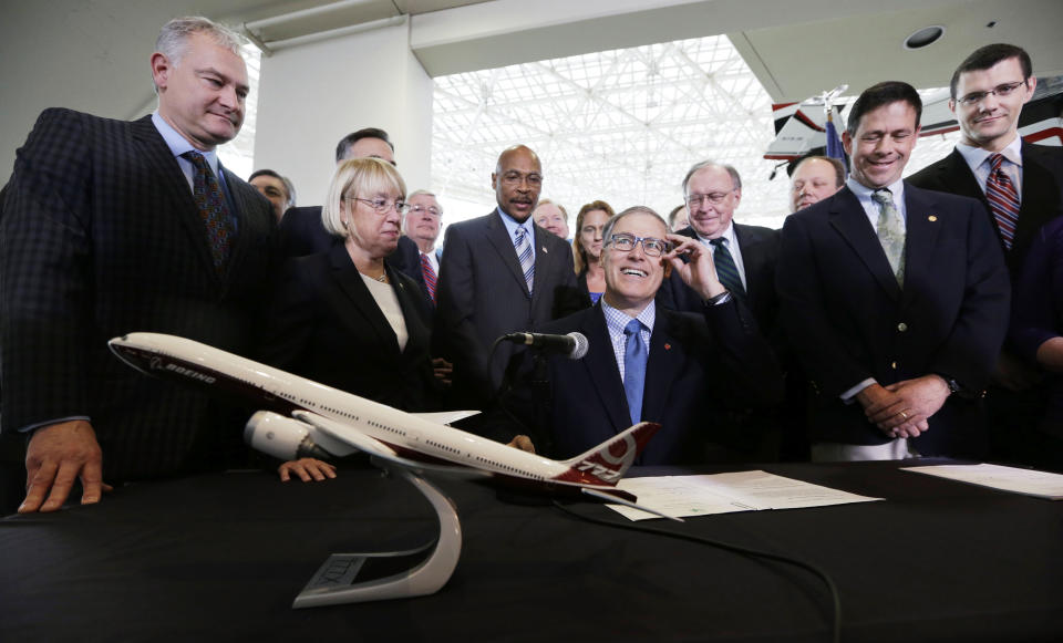 File - In this Nov. 11, 2013 file photo Washington Gov. Jay Inslee, center, adjusts his glasses as he prepares to sign legislation in Seattle to help keep production of Boeing's new 777X in Washington. Lawmakers approved nearly $9 billion of tax breaks for the new jetliner and just a few days later, union members rejected the contract. The Chicago-based company said it would look elsewhere and now has more than a dozen states hoping Boeing will select them as the assembly site of the new 777X. (AP Photo/Elaine Thompson, File)