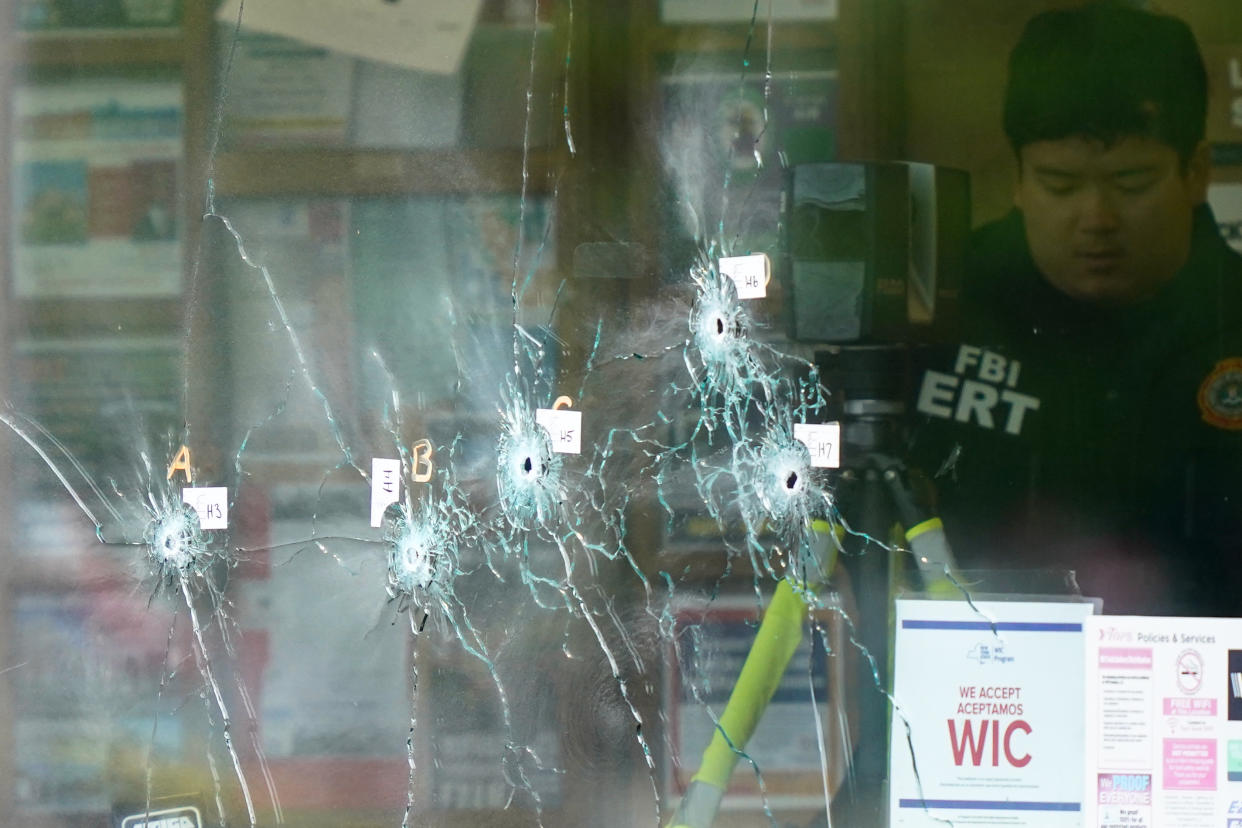 An investigator, next to glass marked by bullet holes, at the scene of a shooting in Buffalo, N.Y.
