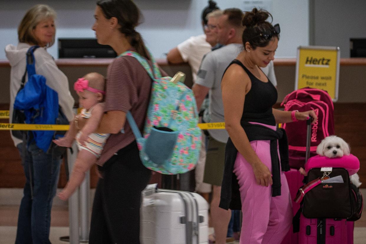 Daisy Reis and her Maltese, Angel, both of Boston, wait in a car rental customer queue across from baggage claim on the ground floor common area as travelers to and from south Florida move through Palm Beach International Airport.