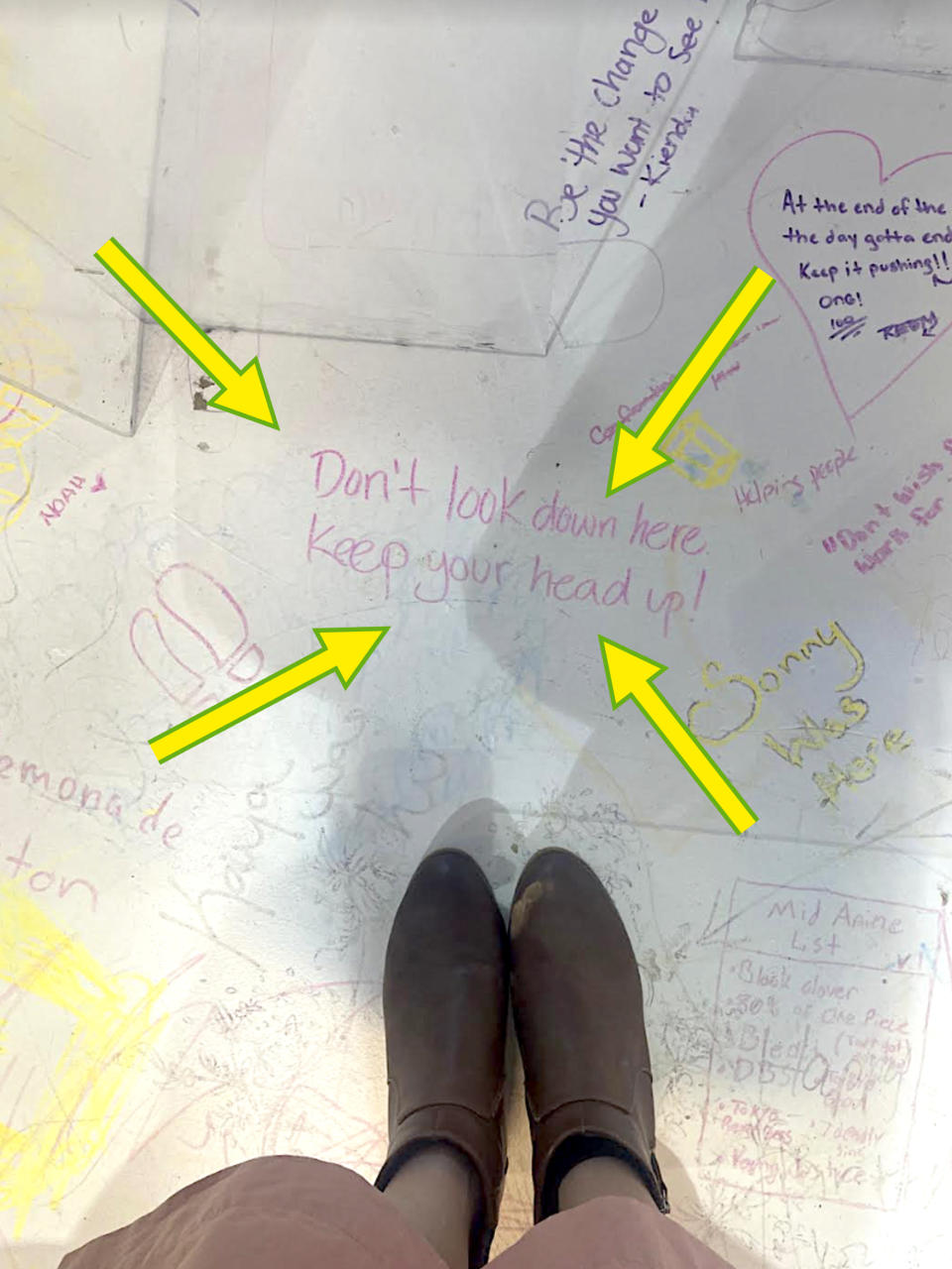 Person standing on a surface covered with positive handwritten messages, including "Don't look down here, keep your head up!" and "Be the change you wish to see - Gandhi."