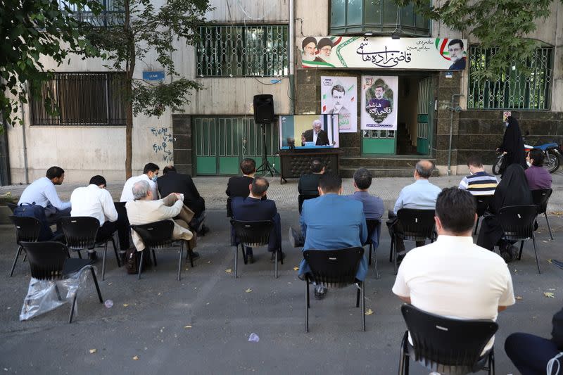 People watch the debate of presidential candidates on a street in Tehran