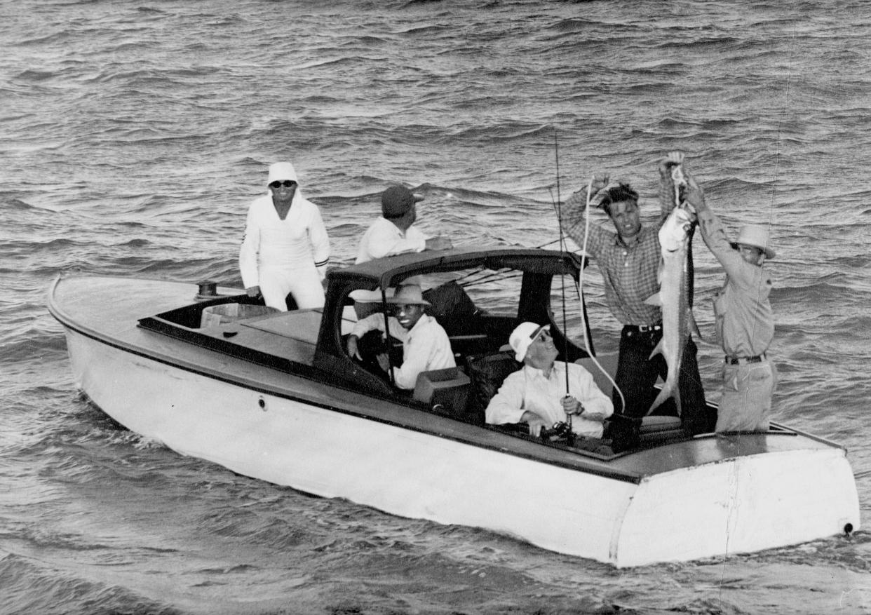 President Franklin D. Roosevelt admires his first tarpon catch off the south jetty of Port Aransas, Texas on May 3, 1937. The president's son, Elliot Roosevelt, and Port Aransas fishing guide Barney Farley (with hat) hoist the silver king up for photographer Doc McGregor to capture, as Don Farley (with zinc oxide on his nose and lips) pilots the boat. They were accompanied by Roosevelt's military attaché Paul Bastedo (white hat) and military aide Edwin Watson (dark hat).