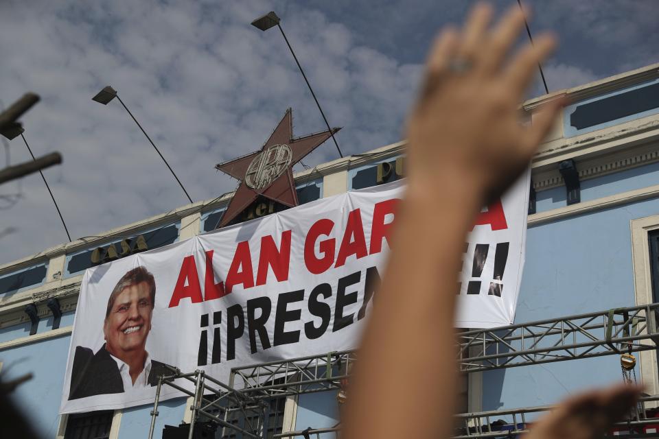 A supporter waves his hand in front of photo of Peru's late President Alan Garcia that reads in Spanish "Present!" during his funeral procession in Lima, Peru, Friday, April 19, 2019. Garcia shot himself in the head and died Wednesday as officers waited to arrest him in a massive graft probe that has put the country's most prominent politicians behind bars and provoked a reckoning over corruption. (AP Photo/Martin Mejia)