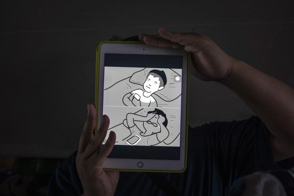 A man holds an iPad with a two-panel comic. Top panel shows a man looking at a phone. Bottom panel shows the man weeping.