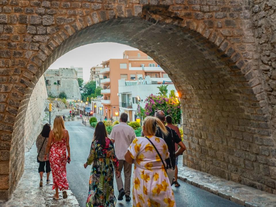 People walk through an archway leading to a colorful, busy street.