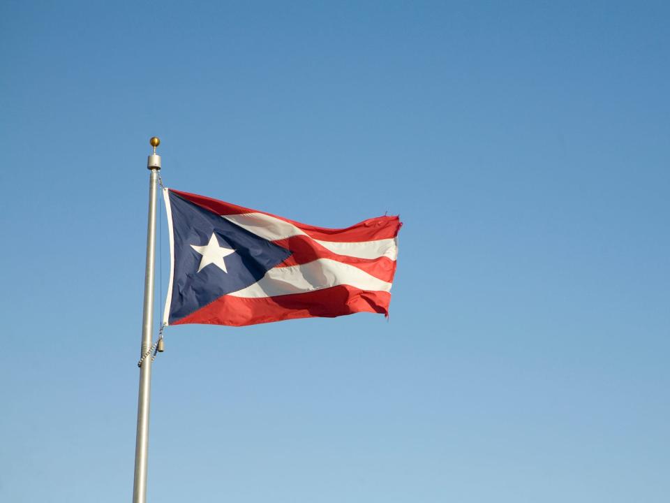 A red, white, and blue Puerto Rican flag waves in front of a blue sky.