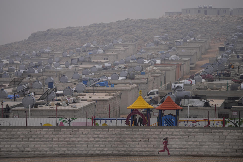 A Syrian young girl runs next to a wall in a refugee camp for displaced people run by the Turkish Red Crescent in Sarmada district, north of Idlib city, Syria, Friday, Nov. 26, 2021. Row upon row of tents, brick homes and other structures with water tanks on top dot the town of Sarmada near the border with Turkey, making up a series of huge informal refugee camps. Women cook, children play, men go to work, pray and discuss politics. Most of the inhabitants are displaced from various bouts of violence in Syria's 10-year conflict. (AP Photo/Francisco Seco)