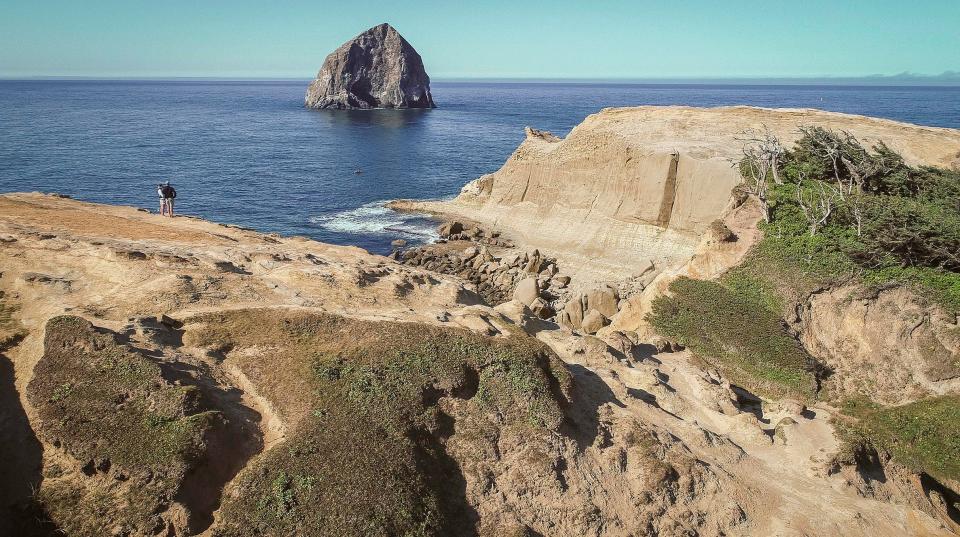 Visitors stand out on a rock to take in views of Cape Kiwanda State Natural Area. Where they are standing is not illegal, but it is beyond a barrier fence that rangers would prefer visitors to the park not cross.