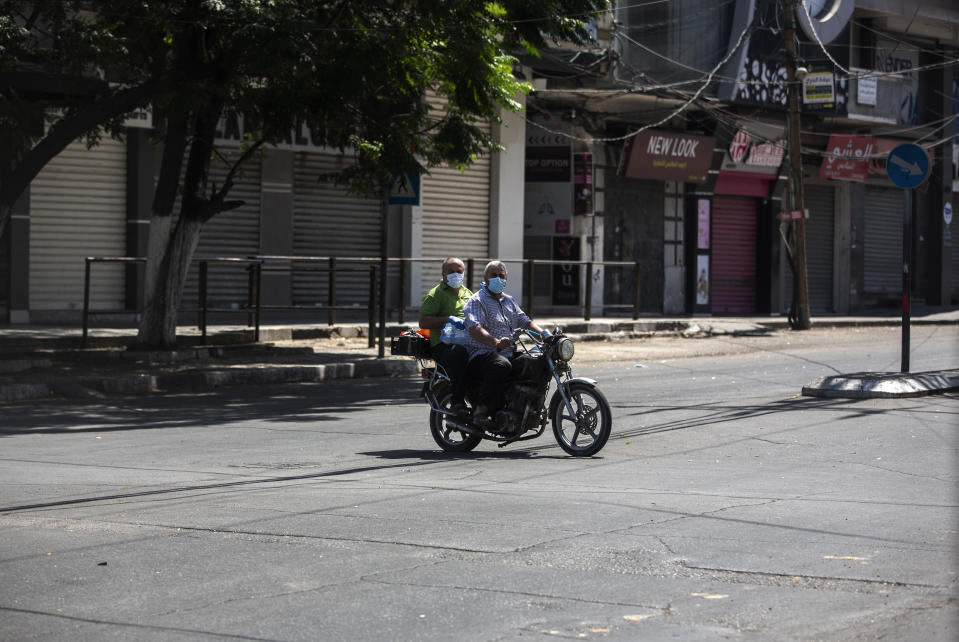 Two Palestinians wearing face masks cross an empty street on a motorcycle, in Gaza City, Thursday, Aug. 27, 2020. On Wednesday Gaza's Hamas rulers extended a full lockdown in the Palestinian enclave for three more days as coronavirus cases climbed after the detection this week of the first community transmissions of the virus in the densely populated, blockaded territory. (AP Photo/Khalil Hamra)