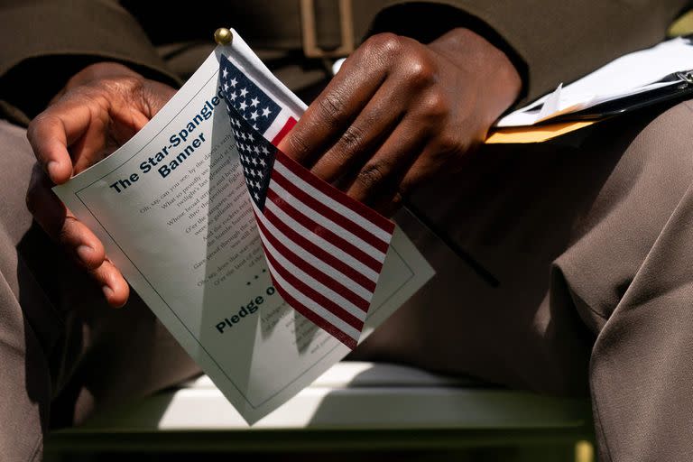 Un nuevo ciudadano estadounidense sostiene la bandera de Estados Unidos y la letra del himno nacional, 