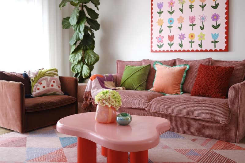 White living room with rose colored sofa, pink and red coffee table, and pink, blue and red patterned rug