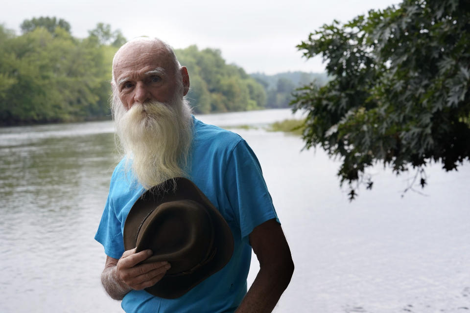 FILE — David Lidstone, 81, known to locals as "River Dave," stands for a photograph near the Merrimack River, Tuesday, Aug. 10, 2021, in Boscawen, N.H. A warrant has been issued for the arrest of the former hermit in New Hampshire who is charged with trespassing on the wooded property he made his home for 27 years after he didn't show up for his arraignment. A prosecutor said Monday, March 7, 2022, the state of New Hampshire has had no contact with 81-year-old David Lidstone on the misdemeanor charge. (AP Photo/Steven Senne, File)