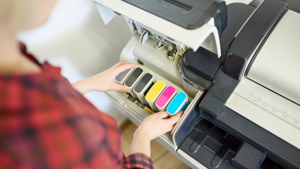 From above shot of anonymous woman putting set of ink into plotter in printing office.