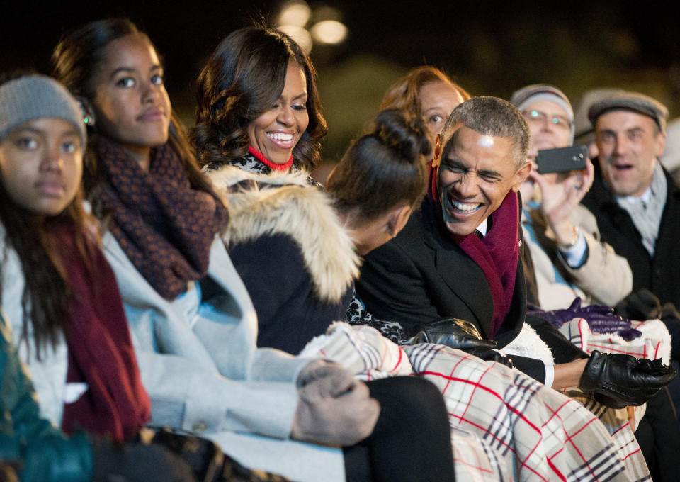 President Barack Obama leans over to talk with his daughter Sasha as they sit with first lady Michelle Obama and Malia and watch the performances at the National Christmas Tree lighting ceremony, Thursday, Dec. 4, 2014, on the Ellipse near the White House in Washington.