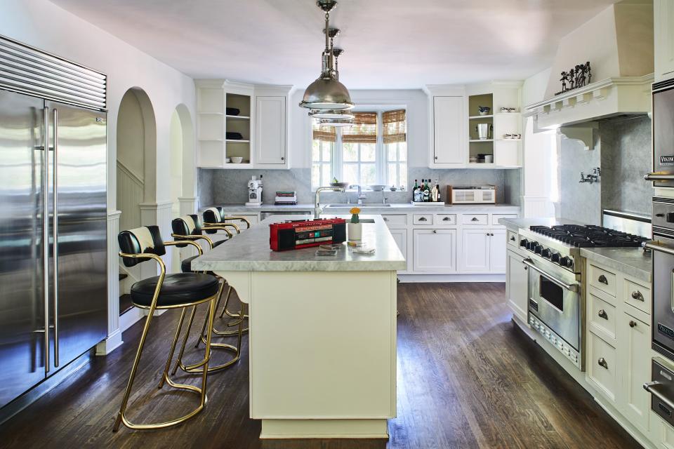 The kitchen was one space Ronson barely touched. “It was just so beautiful as it is,” says the artist. “I remember just walking in and feeling just how spacious and airy it is. Whenever I have people over, they always seem to huddle around that island. It’s so conducive to chatting and bonding.” He re-covered the vintage chairs to match the black-and-white scheme in the breakfast area. Carrara marble tops and Viking appliances remained as is. The stairway to the left takes you the “back way” to the second floor, while a doorway to the right takes you directly onto a covered patio used for hosting and entertaining.