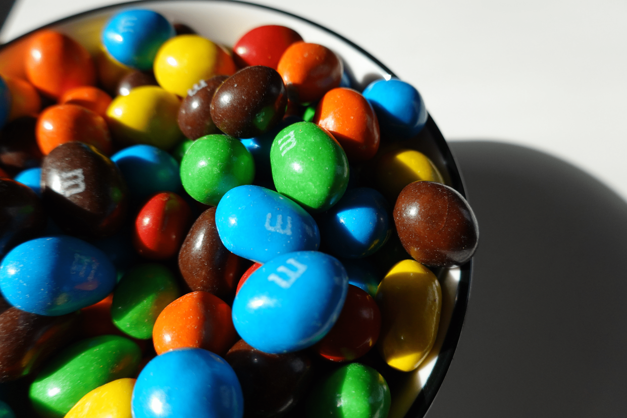 Closeup of peanut M&Ms in a ceramic bowl, dramatic lighting with shadow to the right, on a white table