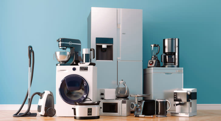 a group of appliances in front of a blue wall, including a washing machine, a refrigerator, a microwave and more