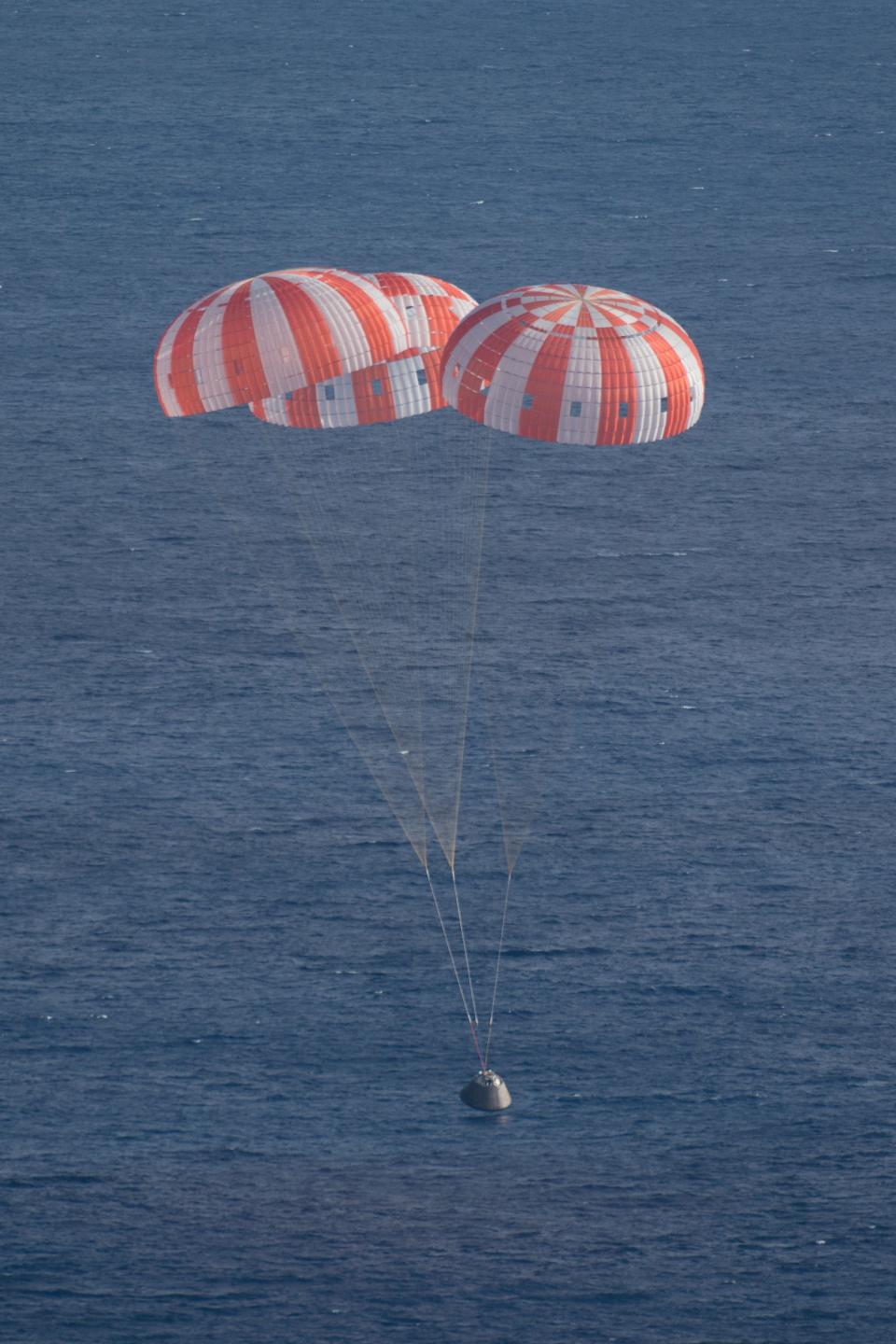 three red and white striped parachutes above a spaceship landing in the ocean